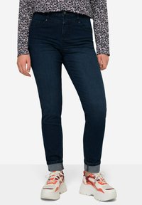 Jeans de tiro alto en azul oscuro, con un diseño ajustado y puños enrollados, combinados con zapatillas blancas gruesas con detalles en naranja.