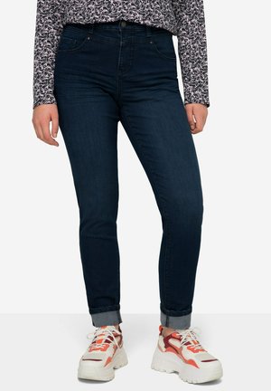 Jeans scuri a vita alta con un design aderente e orli arrotolati, abbinati a sneakers bianche chunky con accenti arancioni.