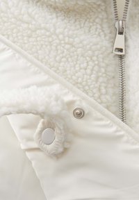 Witte fleece gevoerde jas met een gladde buitenkant, zilveren rits en drukknoopdetails. Voorzien van een zachte, gestructureerde binnenvoering.