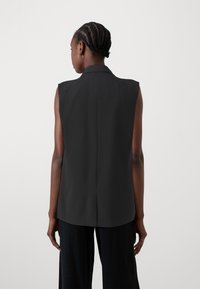 Ärmellose schwarze Bluse mit Kragen, tailliertem Schnitt und glatter Textur. Verfügt über eine dezente Rückennaht und keine sichtbaren Verschlüsse.