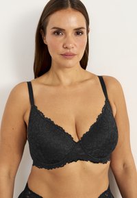 Musta pitsinen rintaliivi, jossa on kukkakuvio, tukeva langanveto, säädettävät hihnat ja aaltoilevat reunat. Pehmeä pinta syvällä V-muotoisella designilla.