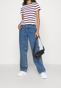 Camiseta de rayas blancas y marinas de manga corta, combinada con vaqueros de denim azul de pierna ancha y zapatillas blancas. Se incluye un pequeño bolso cruzado negro con una correa de cadena.