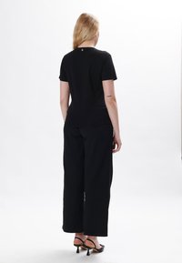 Schwarzes T-Shirt mit kurzen Ärmeln und rundem Halsausschnitt, kombiniert mit lockeren schwarzen Hosen und schwarzen Absatzsandalen. Schlichte Gestaltung, glatte Textur.
