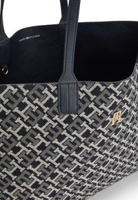 Torebka Tommy Hilfiger z granatowymi skórzanymi uchwytami, wzorzystym materiałowym korpusem i małym złotym emblematem z logo z przodu.