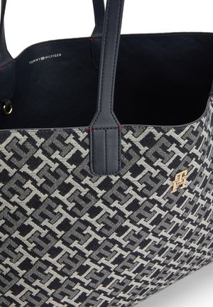 Sac Tommy Hilfiger avec des poignées en cuir bleu marine, un corps en tissu à motifs et un petit emblème en or sur le devant.