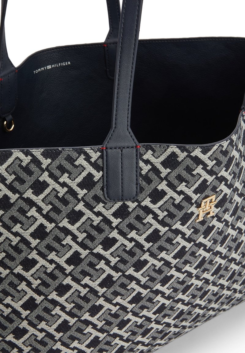 Torebka Tommy Hilfiger z granatowymi skórzanymi uchwytami, wzorzystym materiałowym korpusem i małym złotym emblematem z logo z przodu.