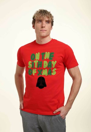 Rød bomulds T-shirt med grøn og sort tekst "PÅ DEN SJETTE DAG AF JUL" og et sort Darth Vader grafisk motiv i midten.