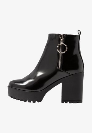 Botines negros de charol con plataforma gruesa y tacón ancho. Cuentan con cremallera lateral y anilla metálica como detalle para facilitar el uso.