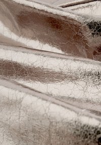 Materiale dalla superficie metallica screpolata di colore argento, con una texture lucida e pieghe e grinze pronunciate. Finitura riflettente.