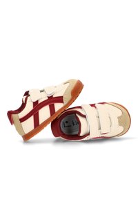 Zapatillas deportivas de velcro en color crema con acentos burdeos. Presentan una suela de goma, una puntera de ante y un forro de tela texturizada.