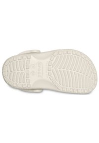 Crocs natikače, bele barve, teksturiran podplat z mrežastim vzorcem, zaobljeni robovi, trak za varno prileganje, lahka zasnova, sproščen stil.