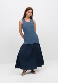 Top sin mangas azul claro acanalado combinado con una falda larga azul oscuro. El conjunto presenta una silueta ajustada con tela fluida.