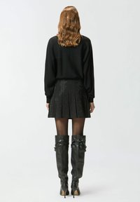 Maglione nero oversize abbinato a una gonna corta plissettata con motivi traforati. Stivali neri al ginocchio in pelle con tacco a spillo.