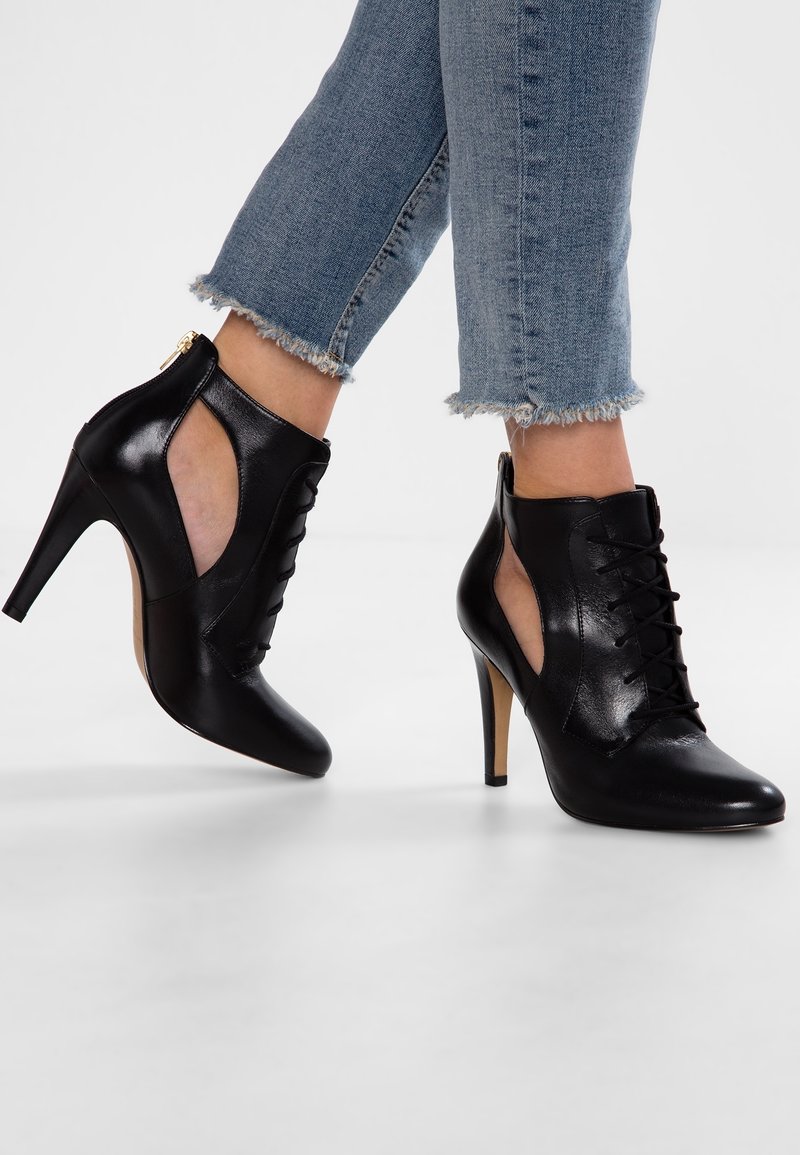 Musta nahkainen nilkkuri, jossa on korkeat korot, nyöritys edessä, leikatut sivut ja sileä pinta. Kengässä on ohut piikkikorko.