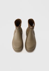 Botas de tobillo impermeables marrones con textura lisa, paneles laterales elásticos y suela reforzada para mayor estabilidad. Diseño minimalista sin adornos.