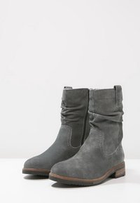 Bottes chelsea en suède gris avec un design décontracté, fermeture éclair latérale, bout rond et petit talon empilé. Présente des accents de couture et une finition texturée.