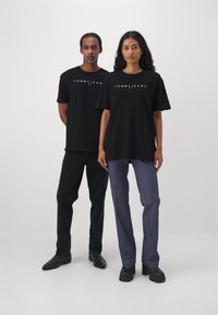 T-shirt in cotone nero con logo "TOMMY JEANS", abbinata a pantaloni neri e blu. Design semplice, vestibilità rilassata, maniche corte.