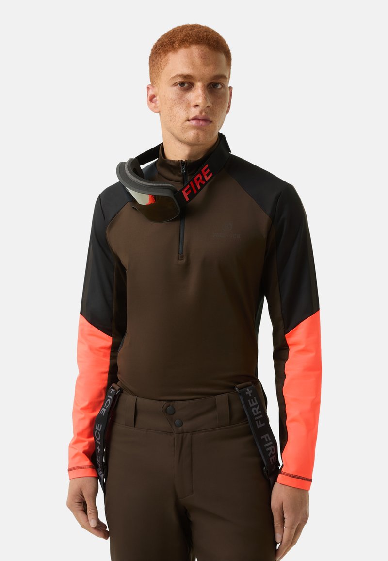 Brown and black long-sleeve top with bright orange accents, featuring a zip neck and "FIRE" printed on the collar. Model wears goggles.