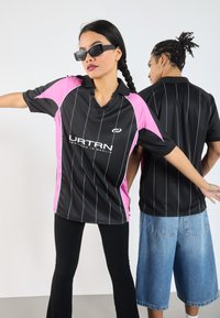 Zwarte en roze sporttruitjes met witte strepen en een kraag, met een logo op de voorkant. Twee personen, één die vooraan kijkt en één die achteraan staat.
