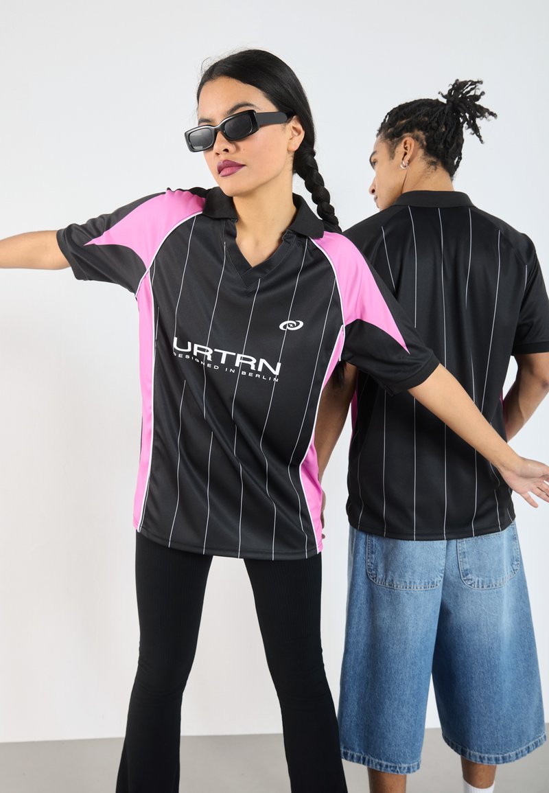 Zwarte en roze sporttruitjes met witte strepen en een kraag, met een logo op de voorkant. Twee personen, één die vooraan kijkt en één die achteraan staat.