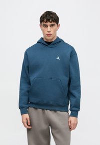 Μπλε φούτερ με κουκούλα από βαμβακερό μείγμα, με μπροστινή τσέπη και λευκό λογότυπο στο στήθος, σε συνδυασμό με ανοιχτό γκρι φόρμα.