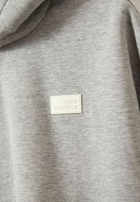 Felpa grigia con un tessuto testurizzato. Presenta un'etichetta crema con testo in rilievo "SOFIE SCHNOOR". Design semplice, senza motivi o decorazioni aggiuntive.