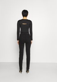 Top negro de manga larga con corte en la espalda, combinado con jeans negros de cintura alta y tacones de aguja negros. Tejido suave, diseño ajustado.