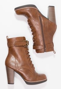 Botas de tobillo marrones hechas de cuero sintético con un tacón grueso, cordones en la parte frontal, cremallera lateral y una correa decorativa con una hebilla de latón.