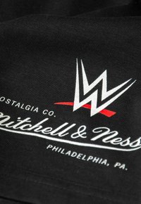 Schwarzer Stoff mit einem weißen und roten Logo. Das Design umfasst ein stilisiertes "W", mit "Mitchell & Ness" in weißer Schrift darunter.