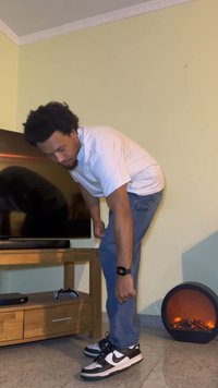 Black and white Nike sneakers, light blue jeans, and a white t-shirt. A black gaming console and controller are on a wooden TV stand.