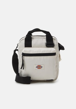 Mała beżowa materiałowa torba na ramię z przednią kieszenią na suwak, czarnym regulowanym paskiem, dwoma uchwytami i naszywką z logo Dickies.