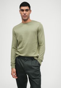 Suéter de punto de manga larga en verde claro con cuello redondo, combinado con pantalones oscuros de corte plisado en gris, textura suave y diseño ajustado.