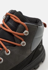 Szare zamszowe buty z pomarańczowymi sznurówkami, srebrnymi oczkami i gumową podeszwą. Posiadają wyściełany kołnierz oraz detale logo na boku.