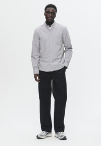 Camisa de botones gris claro con un bolsillo en el pecho, combinada con pantalones negros y zapatillas plateadas. Diseño simple con un corte clásico.