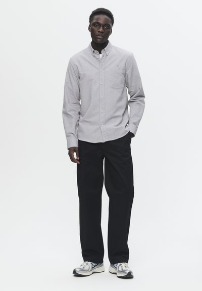 Chemise boutonnée gris clair avec une poche poitrine, assortie à un pantalon noir et des baskets argentées. Design simple avec une coupe classique.