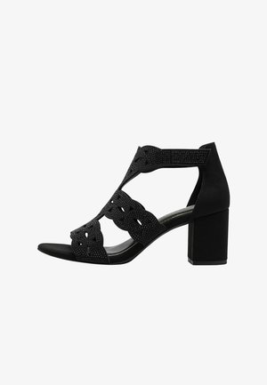 Sandale à talon noir avec un matériau texturé, un design découpé et des embellissements. Caractérisée par un talon épais et un bout ouvert pour une meilleure respirabilité.