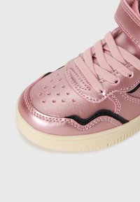 Kuni metallik roosa sneaker perforatsiooni puudutusega varvastel, sobivate paeltega, musta lainemustriga detailiga ja beežist kummist tallaga valge tausta peal.