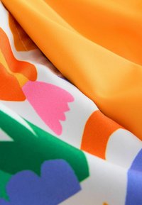 Pezzetti di tessuto multicolore con un tessuto arancione liscio e un materiale bianco con un motivo a fiori in verde, rosa e viola.