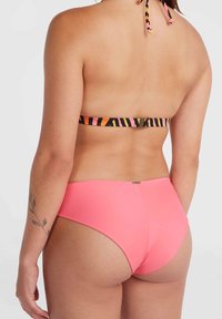 Bas de bikini rose avec une texture lisse ; haut halter à rayures multicolores contrastantes avec fermeture à lien et détail en métal doré.