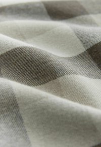 Tkana tkanina w beżowo-brązową kratę, charakteryzująca się miękką teksturą. Materiał ma widoczne detale splotu i lekki połysk.