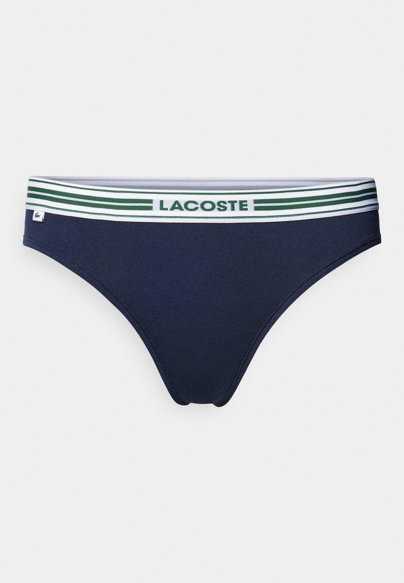Slip navy bleu en tissu doux et extensible. Il présente une ceinture élastique blanche avec des rayures vertes et le logo "LACOSTE" au centre.