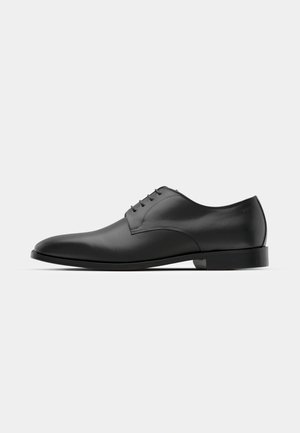 Zapato de vestir de cuero negro con punta redonda, diseño de cordones con cinco ojetes, superficie lisa y tacón bajo y plano.
