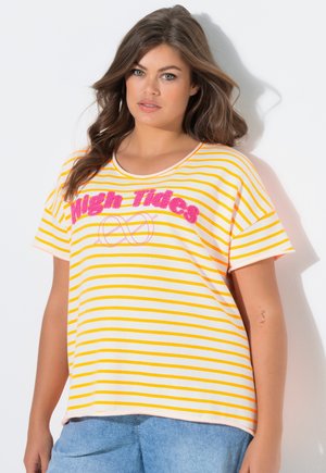 Mujer joven con cabello largo y castaño, vistiendo una camiseta de rayas amarillas y blancas con el texto "High Tides" y jeans azul claro, sobre un fondo blanco.