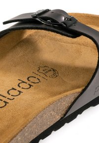 Svart lädersandal med en böjd form, mocka fotbädd och korksula. Har en metallspänne och präglad text på innersulan.