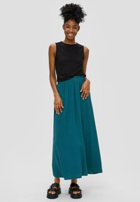 Zwarte, gestructureerde mouwloze top gecombineerd met een vloeiende teal maxi rok. Model draagt chunky zwarte plateauschoenen. Eenvoudig ontwerp met elastische taille.