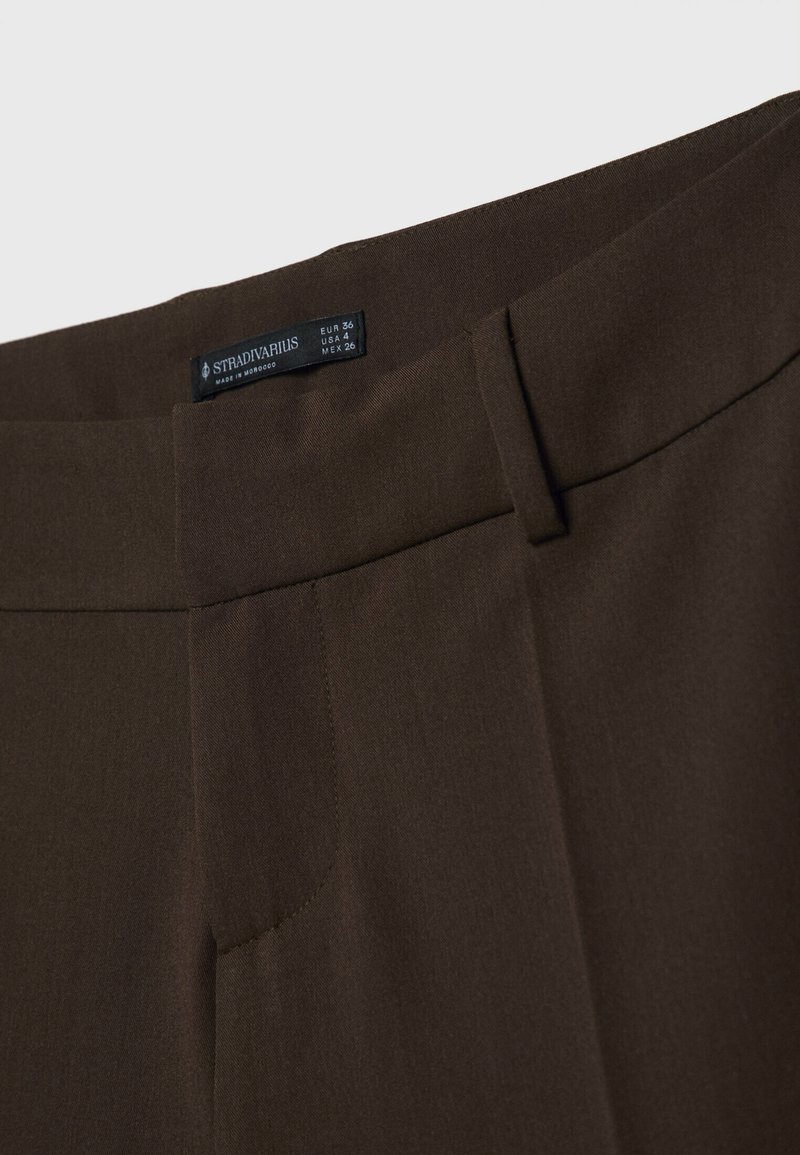 Pantaloni tagliati marroni con una superficie liscia, caratterizzati da un frontale piatto, tasche laterali e l'etichetta Stradivarius visibile sulla cintura.