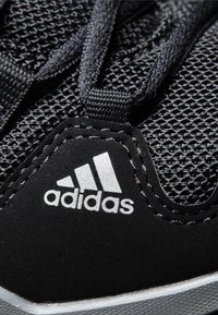 Czarne buty sportowe z siateczkową cholewką, syntetycznymi akcentami i szarym spodem. Posiada czarne sznurowadła i białe logo Adidas.