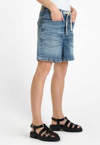Shorts en denim bleu clair avec une coupe décontractée, taille élastique à cordon, deux poches avant et deux poches arrière. Assortis à des sandales noires à lanières.