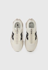 Sneakers with a cream mesh and black synthetic upper, featuring a chunky sole, front lacing system, and prominent branding on the tongue.