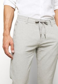 Ljust grå linnbyxor med elastisk midja, dragsko och sidofickor. Tyget har en mjuk, texturerad yta.